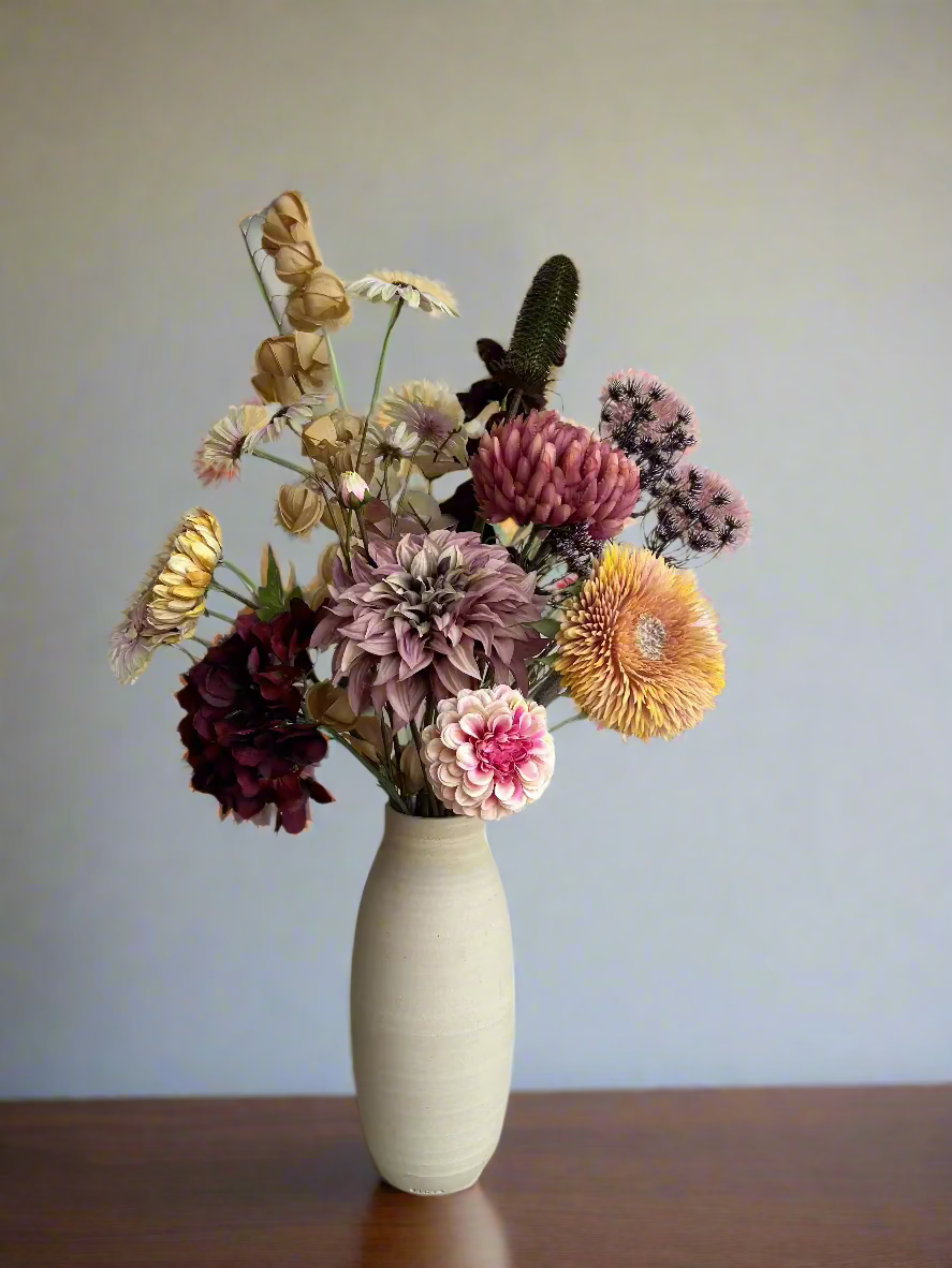 A silk flower arrangement featuring a bouquet with soft yellow, rose, and burgundy hues in a ceramic vase.