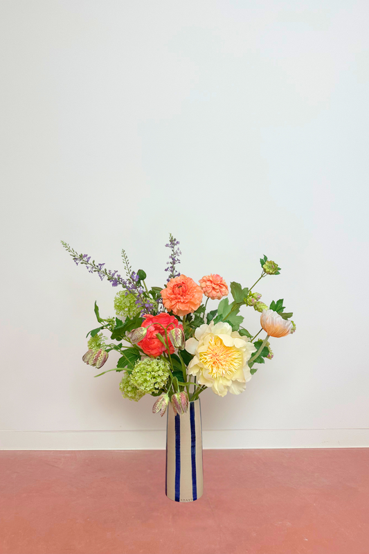 Bouquet of colorful flowers in a striped vase on a pink surface with a white background